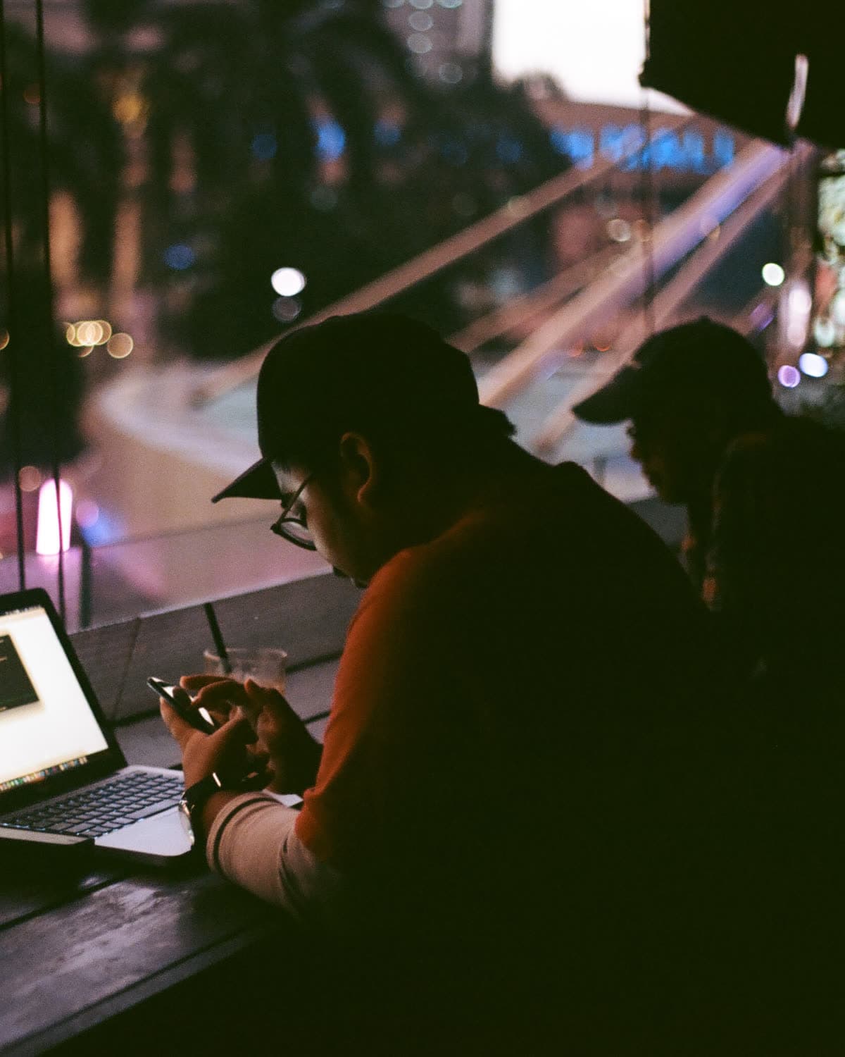 Someone still working at a laptop after dark, city lights in the window behind them